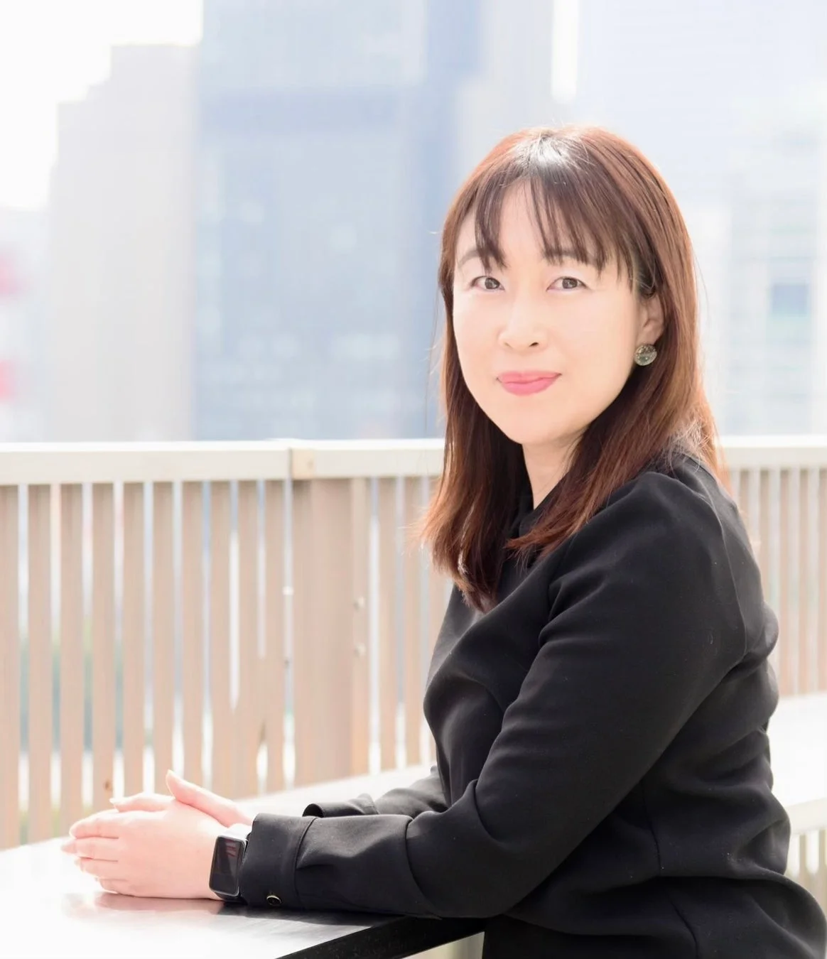 黒いジャケットを着たアジア人女性が屋外でカメラに向かって微笑んでいます。