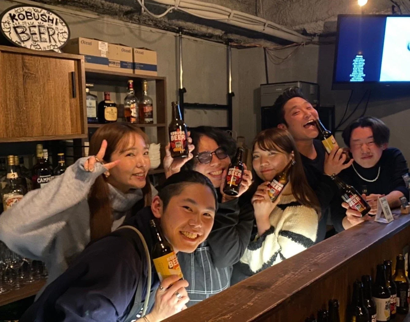 友人たちがバーカウンターで集まり、笑顔でビールを手に楽しんでいます。