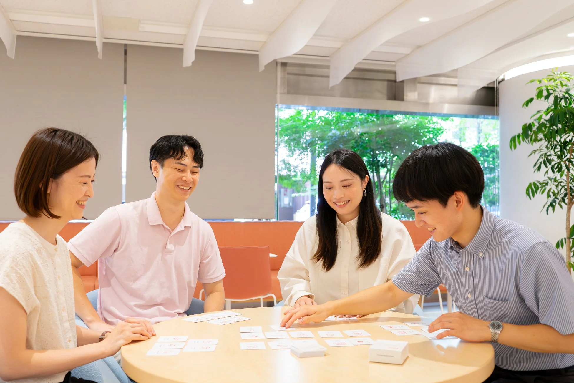 4人の男女が笑顔でテーブルを囲み、カードゲームを楽しんでいます。