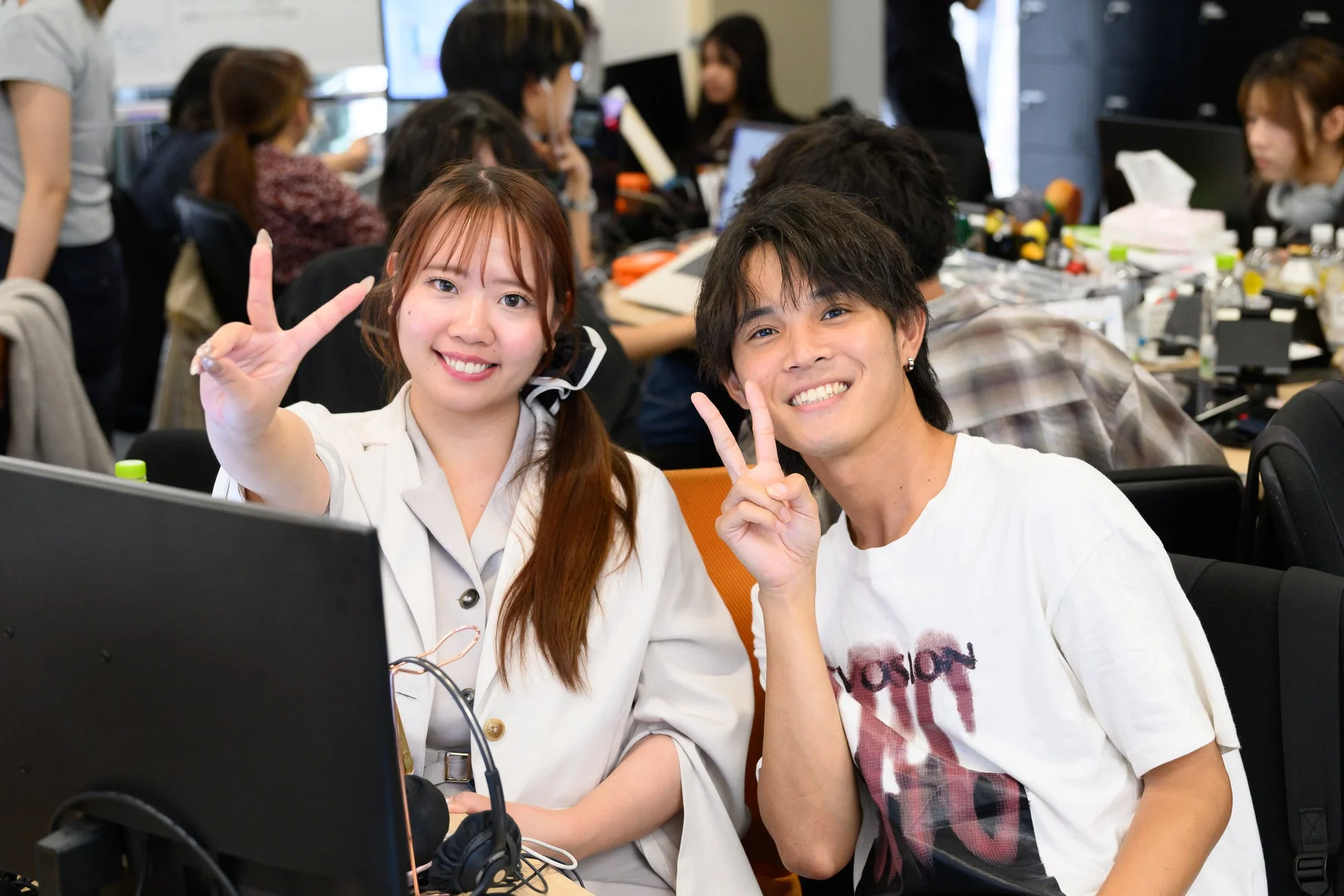 オフィスで笑顔の若い男女がピースサインをしている様子